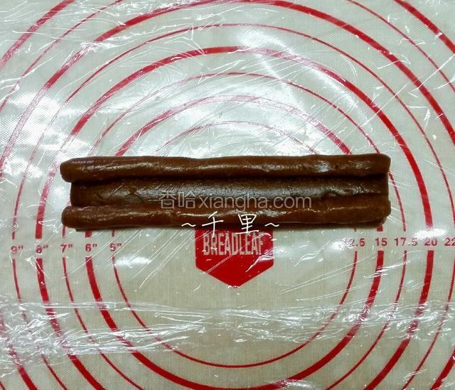 將兩份15克的可可麵團，搓成兩條各15厘米的長麵團，再拼在剛才卷好的麵團上方的兩旁，用保鮮膜包好放冰箱20分鐘讓麵團硬些
