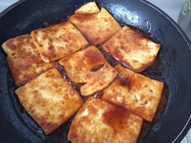 把料汁淋在豆腐片上，晃动平底锅，使料汁均匀裹在豆腐片上；