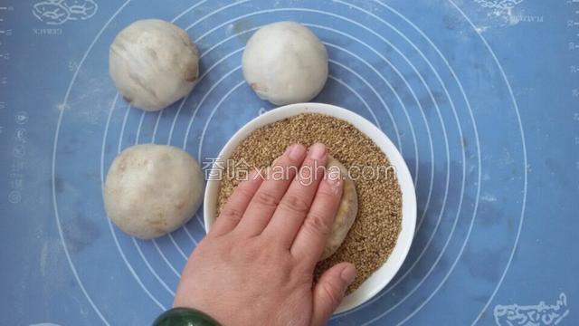 拿一个烧饼生坯按在盛满芝麻的碗里，把烧饼的一面粘匀芝麻，剩下依此类推；