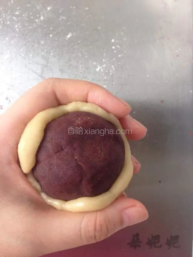 手心拍少许低筋面粉防粘。取一块面皮压扁，再取一块豆沙馅，用虎口和大拇指慢慢往上推，一点点包起来。