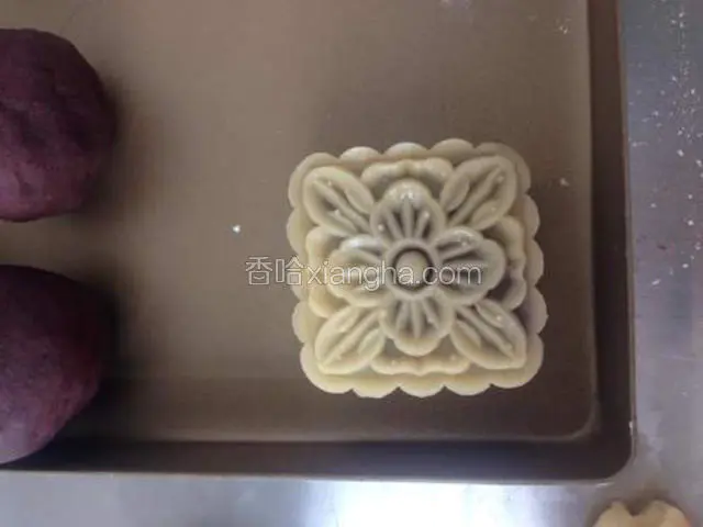 模具倒一些面粉防粘，倒出多余面粉，将搓好的月饼胚压出花纹。每压一个最好都倒一点面粉进模具防粘。