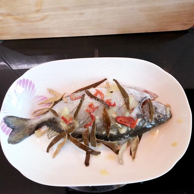 在鱼身两侧划三条浅斜痕、涂抹盐、花生油，上下铺果皮丝蒜蓉及椒丝