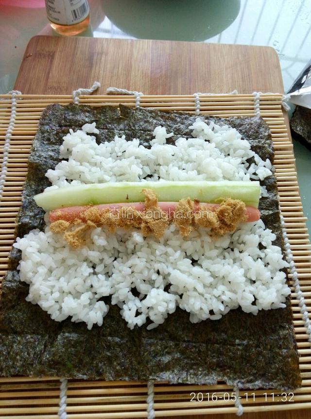 菜板上放好寿司卷，然后放上海苔片，然后放入米饭，然后放入黄瓜肉松火腿。