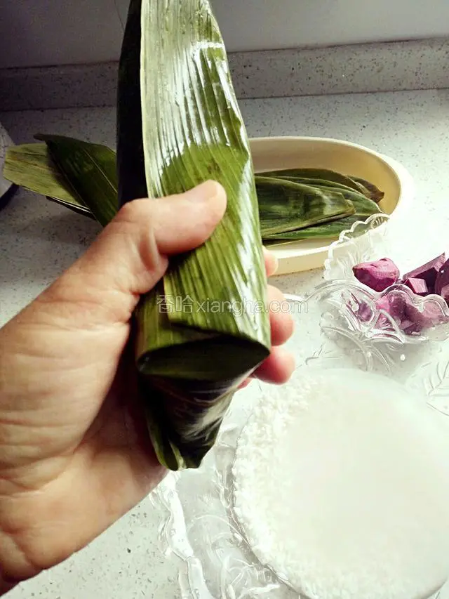 底部添小量米，然后加入密枣，紫薯块，再添米，折粽叶盖住糯米。