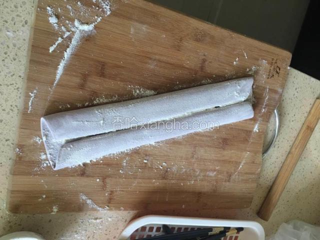 另一端也向中间卷起。卷好后，表面撒薄粉。