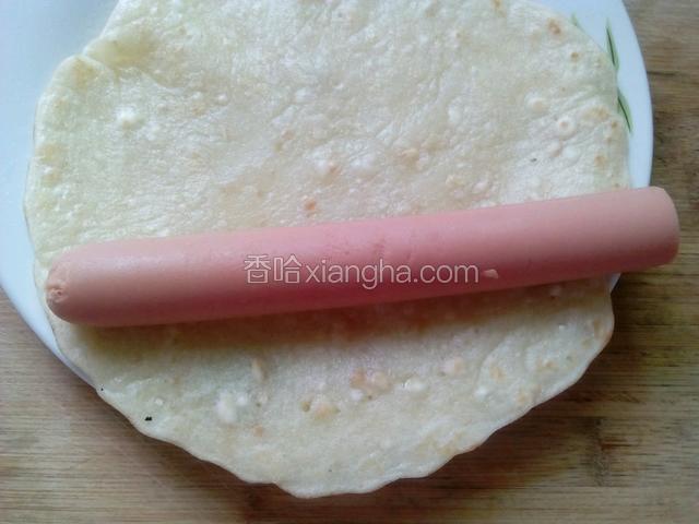 把火腿肠放在煎好的饼上从一边卷起来
