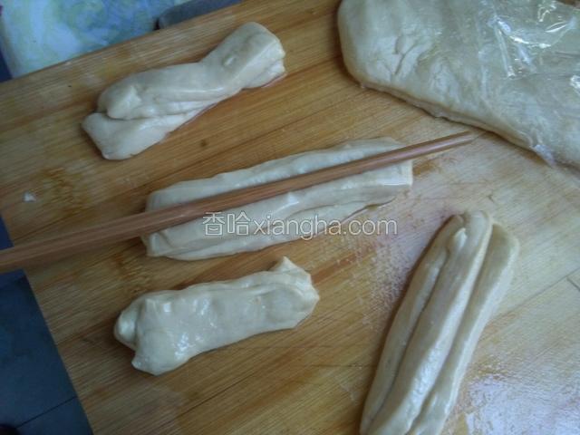 在操作台面上，抹上少许的油，将浸渍好的面团轻轻，拉长放在操作台面上，用手轻轻按扁，用刀将面片成剂子，将剂子叠放在一起，用筷子压一下，捏住两端轻轻拉长。