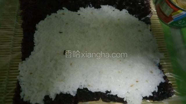 寿司帘上放一张紫菜，将米饭均匀铺好，用饭铲压实，一端留3厘米不放米饭，方便卷起