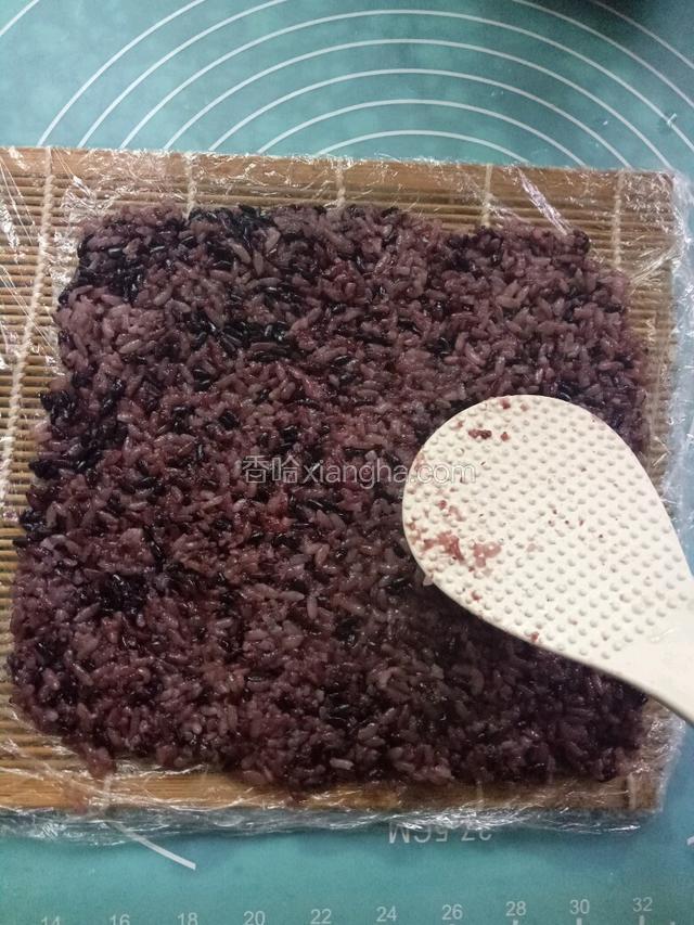 寿司帘包上保鲜膜，在上面平铺一层糯米饭，用勺子压平。