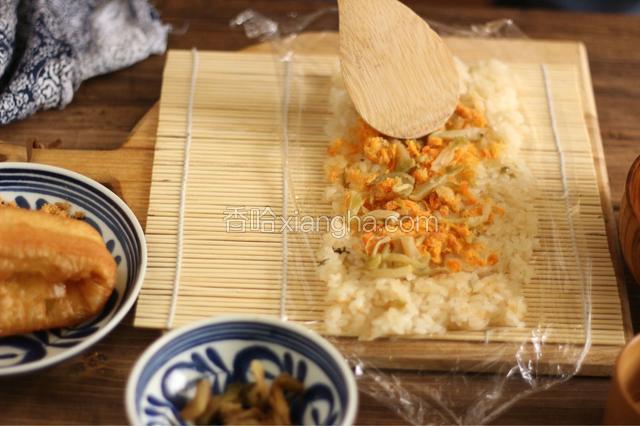 勺子稍沾些水，把米饭均匀铺好。接着铺上榨菜、肉松。