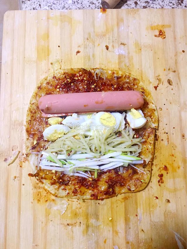 炸好的饼上依次刷甜面酱，蒜蓉辣椒，辣椒油，然后把香肠，熏肉，煮鸡蛋，葱丝，炒好的土豆丝挨着摆放，卷起来就可以吃喽！