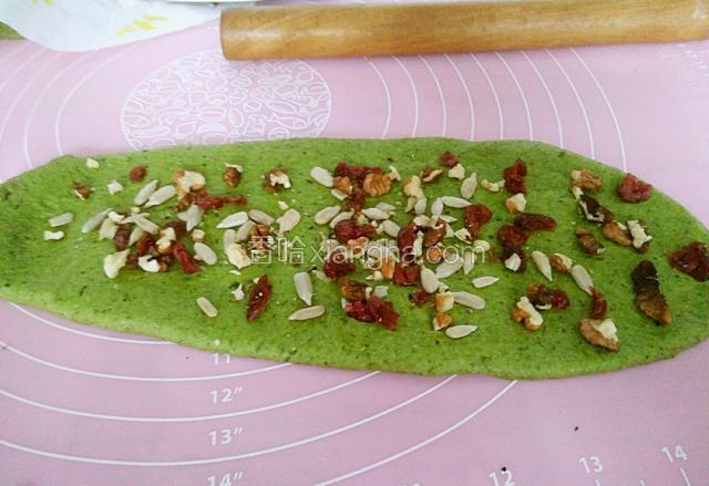 然后将蔓越莓，瓜子仁还有核桃仁，铺在牛舌饼上。用擀面丈压几下