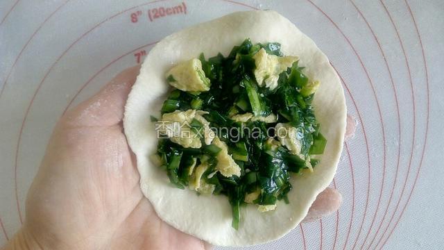 一手轻托饺子皮，另一手用勺子舀适量韭菜鸡蛋馅，放到饺子皮上，