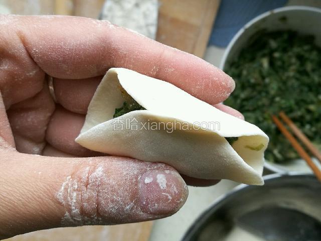 用左手托着饺子，右手拇指和食指把中间捏紧。