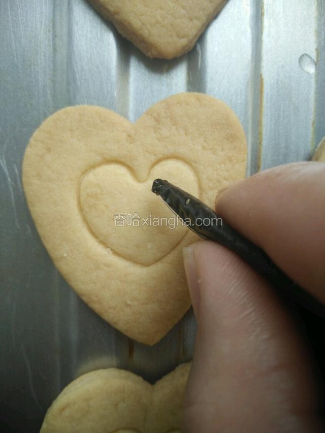 把裱花袋尖那剪个口，烤好后取一个饼干在里面的小心形印的地方用巧克力酱做个装饰，挤完巧克力酱撒上彩珠糖