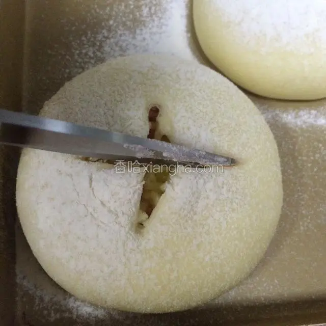 给二发好的面团筛上一层薄薄的面粉，用剪刀在面包表皮上剪个十字的口子。