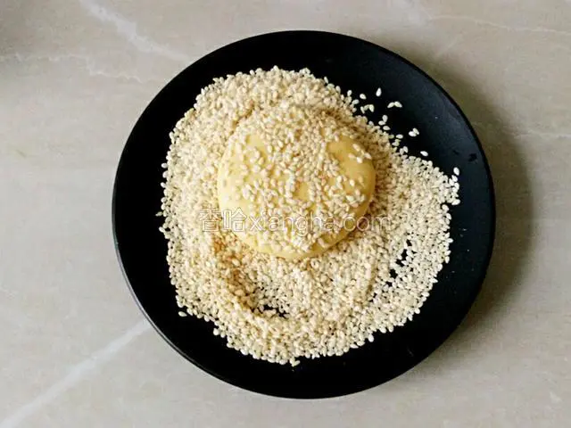 取适量面团搓圆再按压成饼状，沾上白芝麻