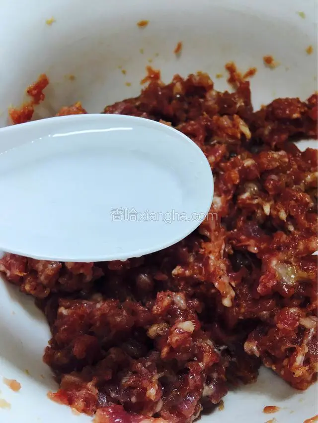 与调料拌匀的肉馅，分三次加入适量清水，顺时针搅拌起胶