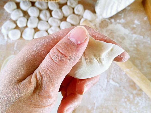 两手中指托住饺子底部，拇指和食指同时捏紧饺子，收口