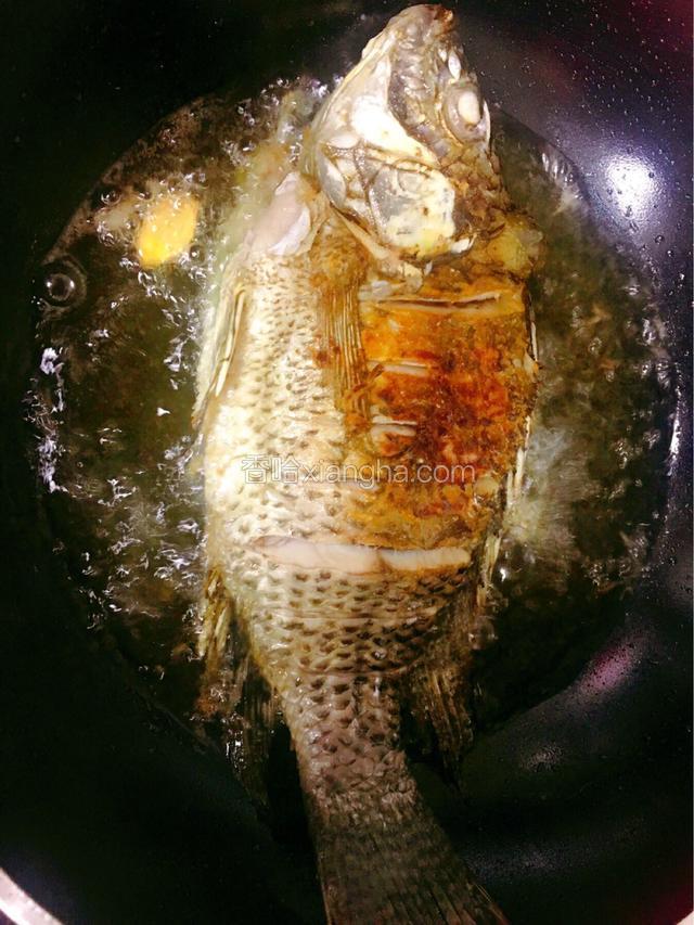 手拎着鱼尾让鱼身上的水尽量留干，再把整条鱼放入油锅大火炸制金黄色，断生后捞出备用