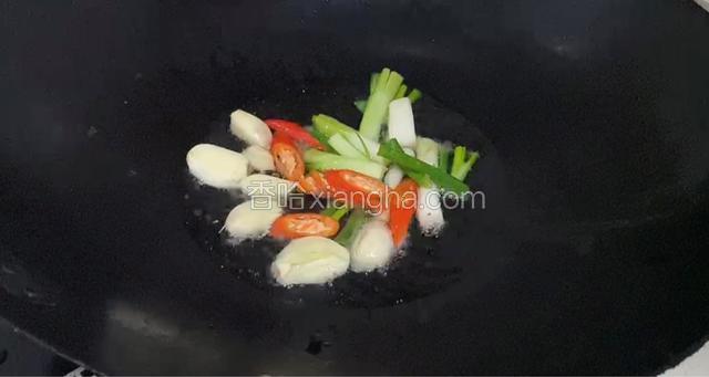 锅中倒入适量油烧热后倒入蒜头，葱段，辣椒丁炒出香味