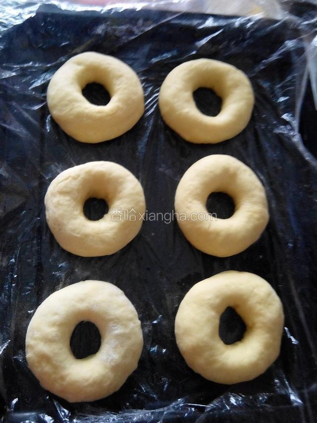 经过手动整理，将有洞的面饼整形成甜甜圈的形状。排入铺有保鲜膜的盘子静置25分钟醒发，上面也松松的盖保鲜膜。