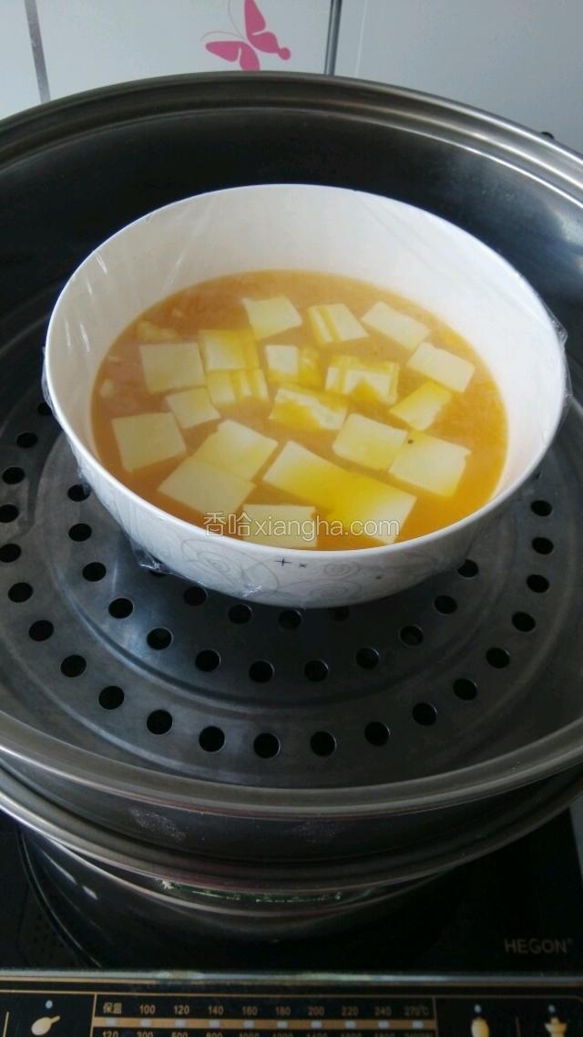把鸡蛋倒入豆腐碗中，并盖上保鲜膜上锅蒸