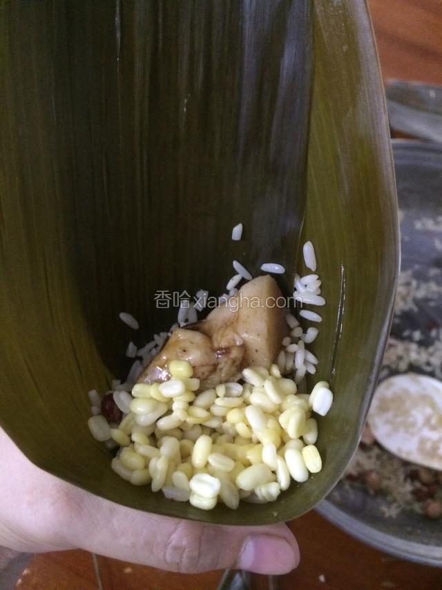 往漏斗粽叶加入一勺糯米，加入适量绿豆和猪肉…