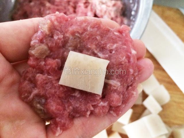 手上沾水，用汤匙挖一块肉馅，放在手指部位，轻拍成薄片状，中间放一小块肉皮冻；