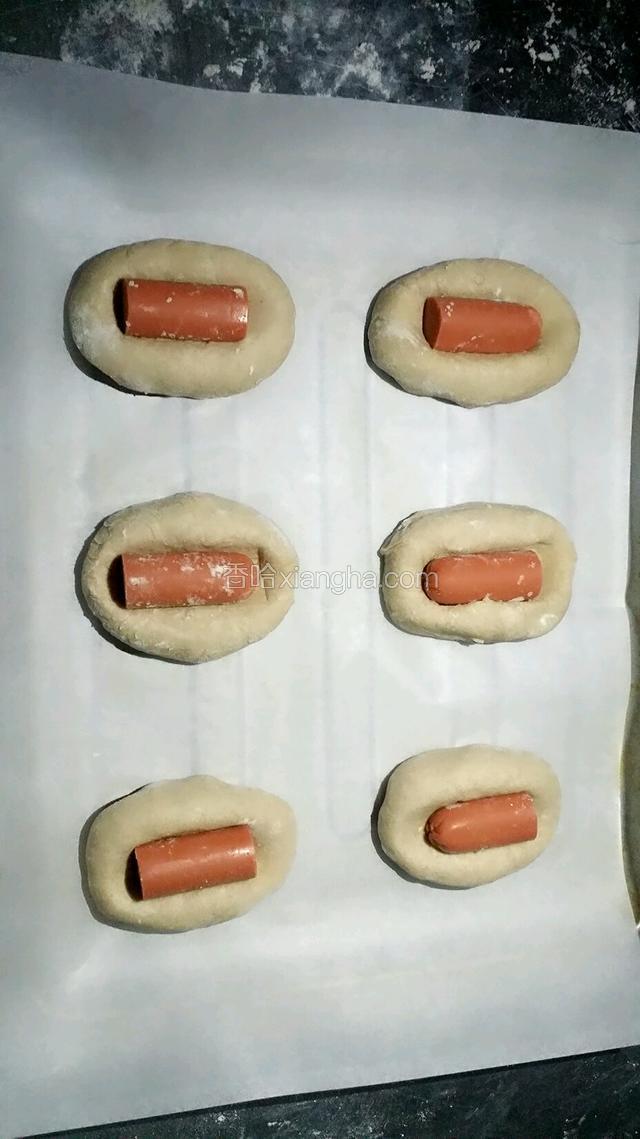 静止好后的面团捏成椭圆形，中间压扁放入切好的火腿肠