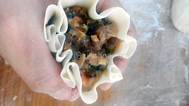 放上馅，用虎口包住烧麦，用另一只手像包包子似的捏出小褶来，捏一圈，口留着。