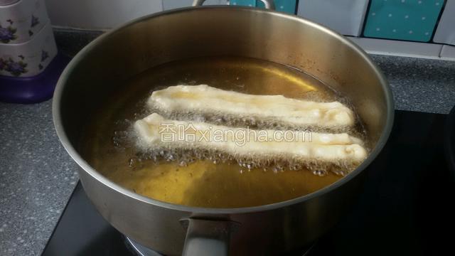 锅中油热后，把油条拉长下锅炸熟