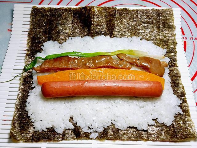 將一块紫菜放在壽司席上，把米飯放在紫菜上，再放上南瓜、香腸、蔥條、牛柳（這是包饀料的米飯只需約占紫菜的2/3就可以了）