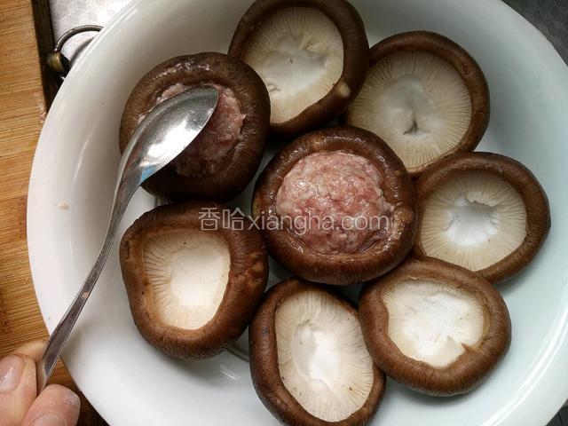 用勺子把肉馅舀到香菇盅里，压紧整型