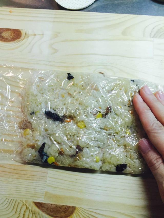取适量摊开在保鲜膜上，保鲜膜要稍微大些，一会儿才好卷饭，用饭勺稍微整形成长方形后，把余出来的保鲜膜盖在糯米饭上，用手压按再整整，让型状成比较接近完整的长方形