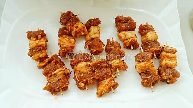 用牙签把腌好的羊肉串起来，每个牙签上面串三四块羊肉，把肥肉和瘦肉穿插开。