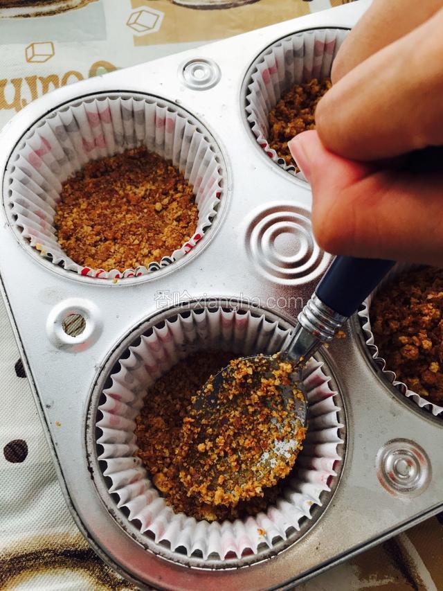 把饼干碎倒入烤盘底部（ 每一个放入一汤匙半的饼干碎）。然后用汤匙按压知道表面平紧。最后放入冰箱冷藏备用