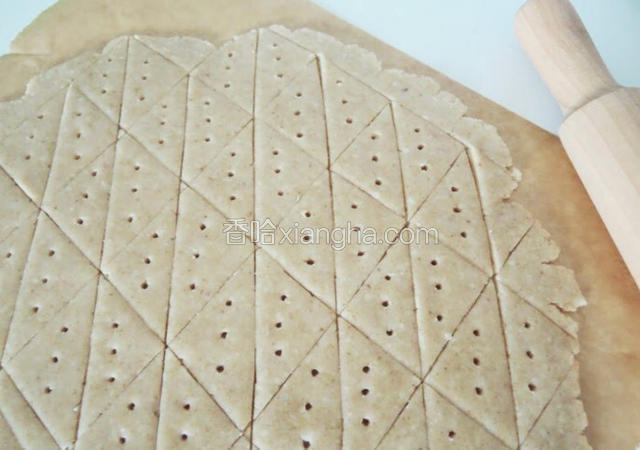 此时预热烤箱，上下火160度。
然后将面团包上保鲜膜，擀成大约4mm薄，用刀子成三角形，再拿叉子在上面扎一下，造型就完成了。