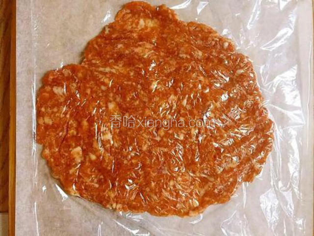 将和烤箱大小一致的油纸铺在台面上，取大概1/4的肉馅放在油纸上，害保鲜膜后用擀面杖擀成薄薄的片状。