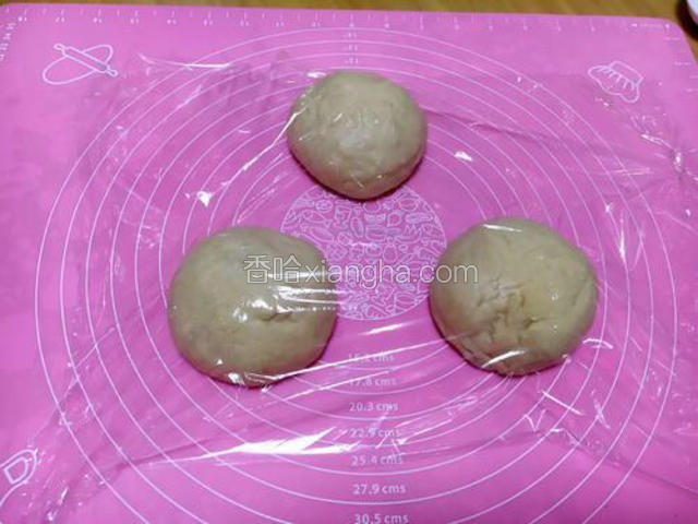 把面团中的空气挤出，把面团分成3份，揉圆并放在室温条件下醒发20分钟，盖上保鲜膜。