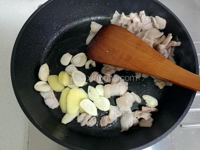 等五花肉煸炒出油，变色，用铲子把肉堆到一边，加入姜和蒜煸炒。