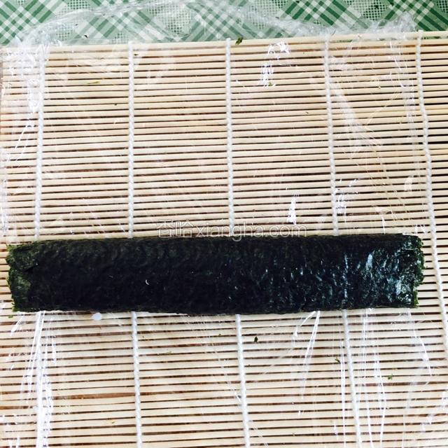 用保鲜膜和卷帘将海苔卷起来，一点一点卷，保鲜膜和卷帘向前拉一下卷一下，用劲卷实