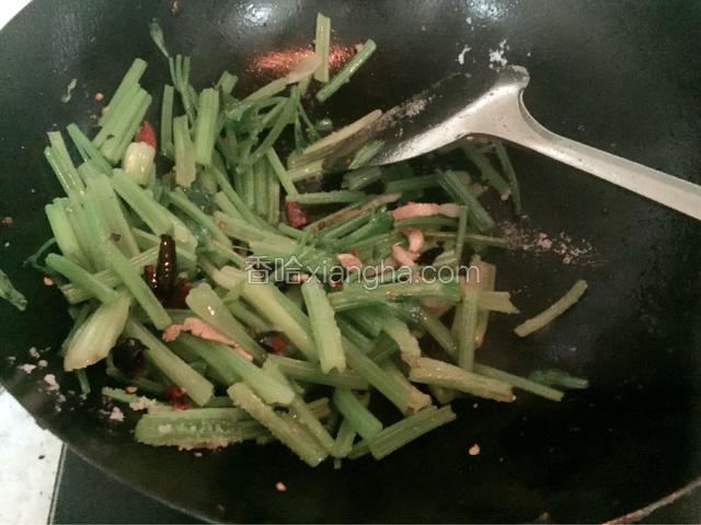 下入芹菜，不停翻炒，出水变软后，添加盐。