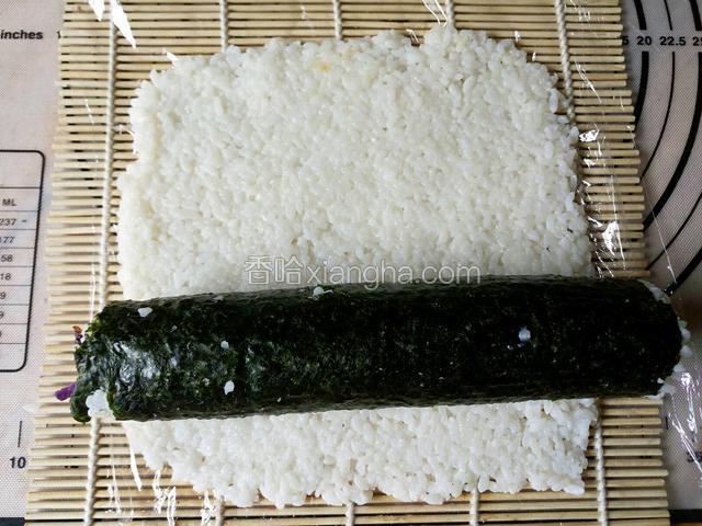 放上刚才卷好的紫菜卷，同样先包裹一圈内部材料，再利用寿司帘带动着。