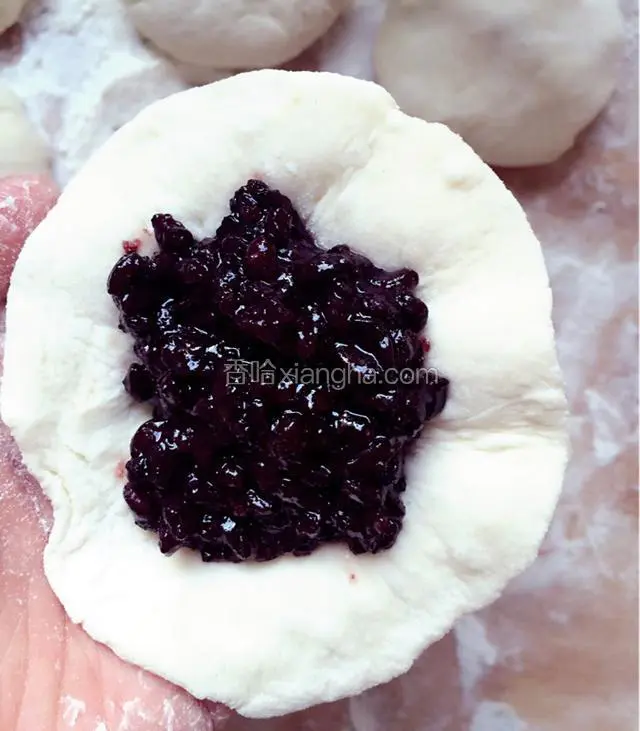 取一个剂子，用擀面杖擀成边缘薄，中间略厚的面饼，中间放紫米饭做馅儿；