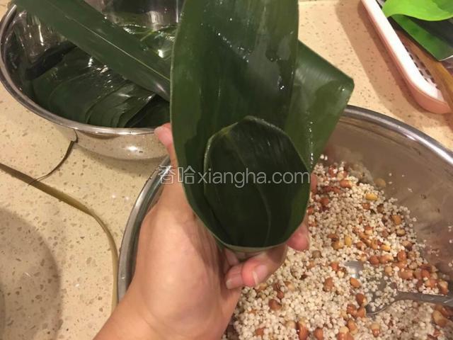 在粽叶根部的1／4处把粽叶折成漏斗形状。