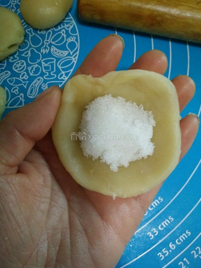 将小面团按扁，用擀面杖轻擀两到三下，包入白糖，用包包子的方法捏紧收口，收口朝下摆放。