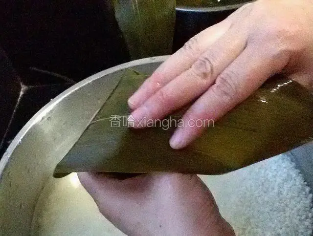 一只手把粽子握成三角形，另一只手把上面粽叶盖下来。