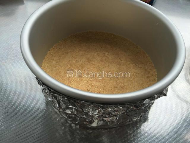 六寸圆模包上锡纸，把拌好的消化饼沫铺在模具底部，用勺子压平压实，放进冰箱冷藏