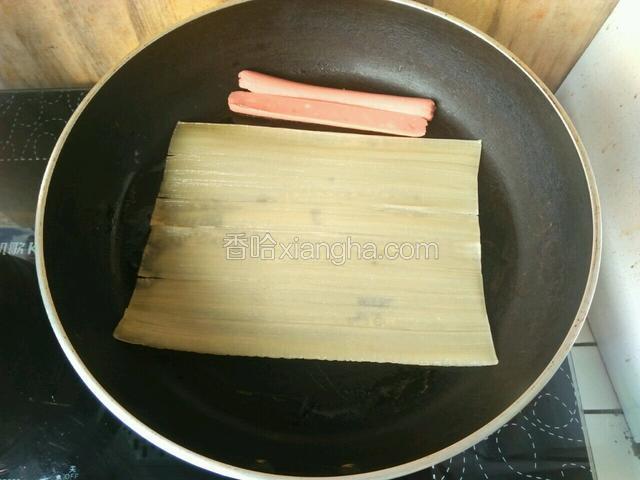 平底锅热锅，用刷子刷上一层油，将冷面放进去，火腿肠也放进去煎一下，冷面上要用刷子刷点水